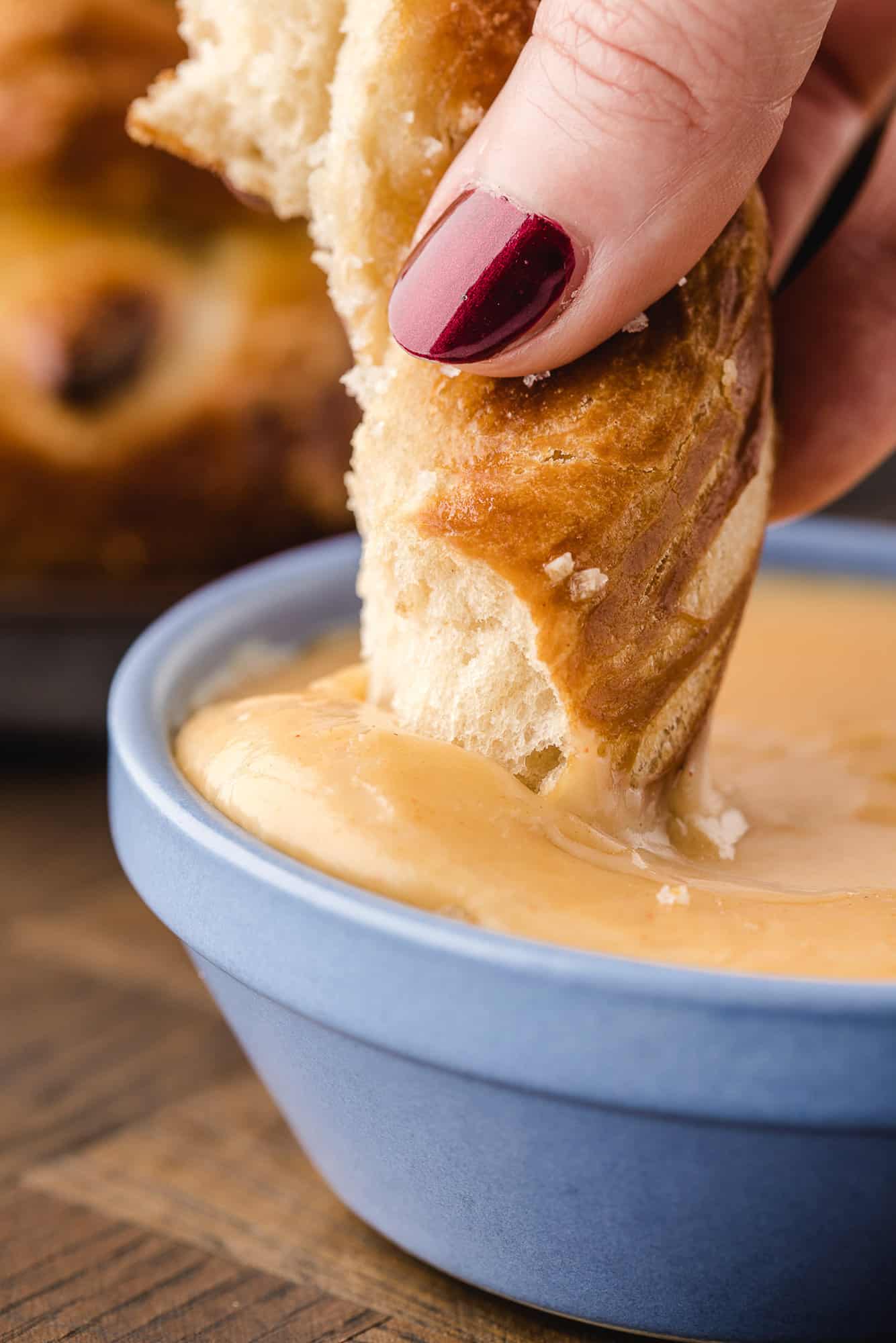 Pretzel being dipped into cheese sauce.