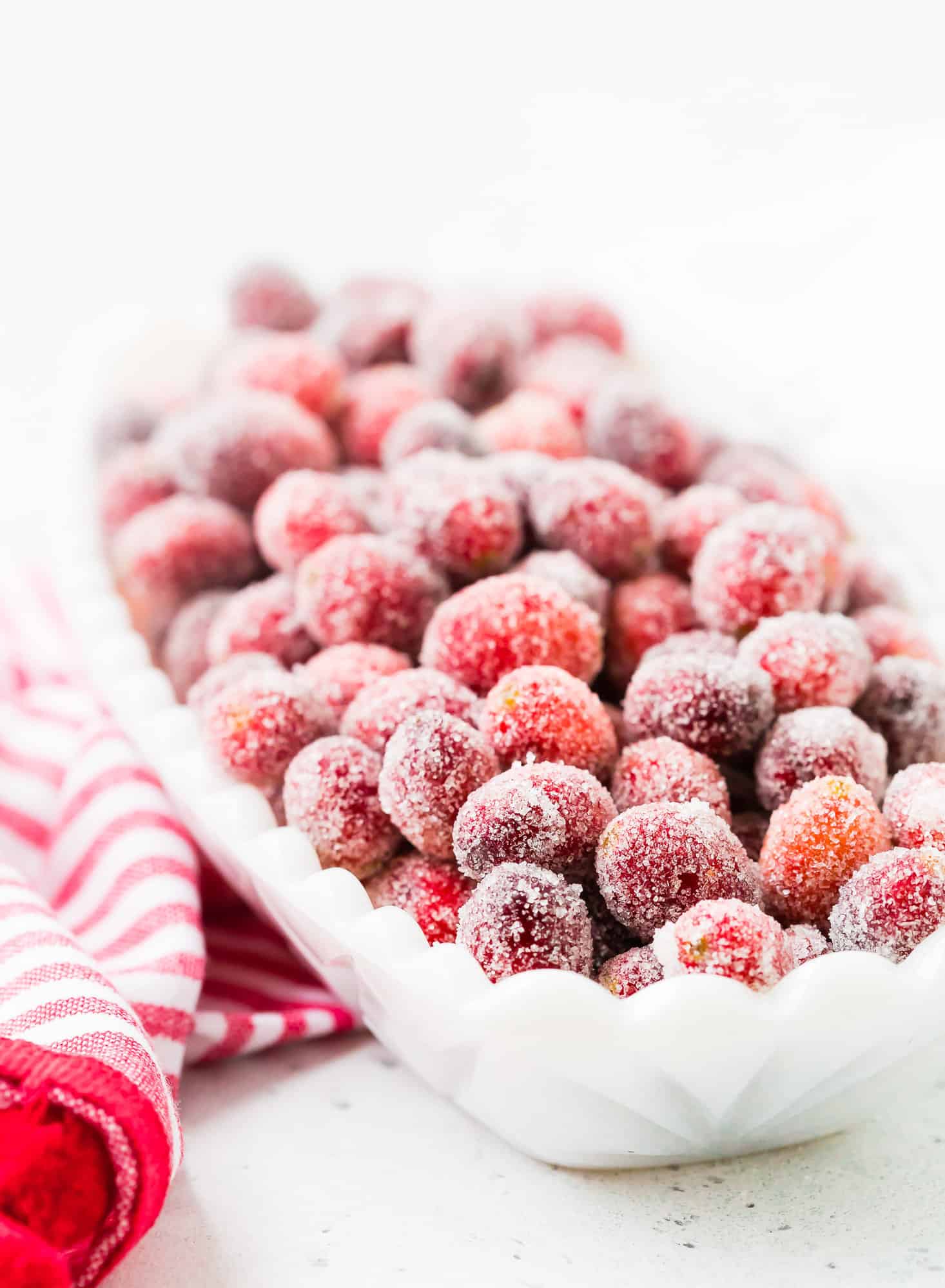 Candied cranberries in a white bowl set on a red and white linen.