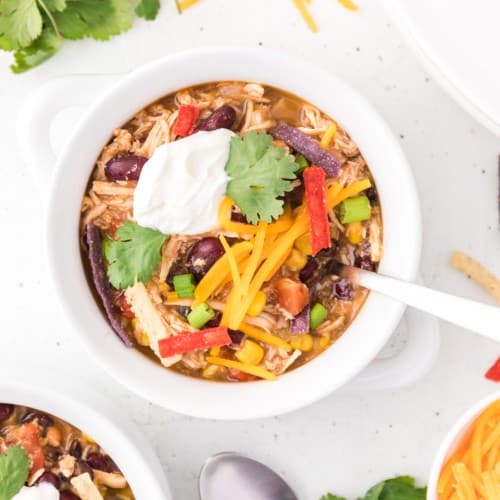 Chicken taco soup in a white bowl, topped with sour cream and cilantro.