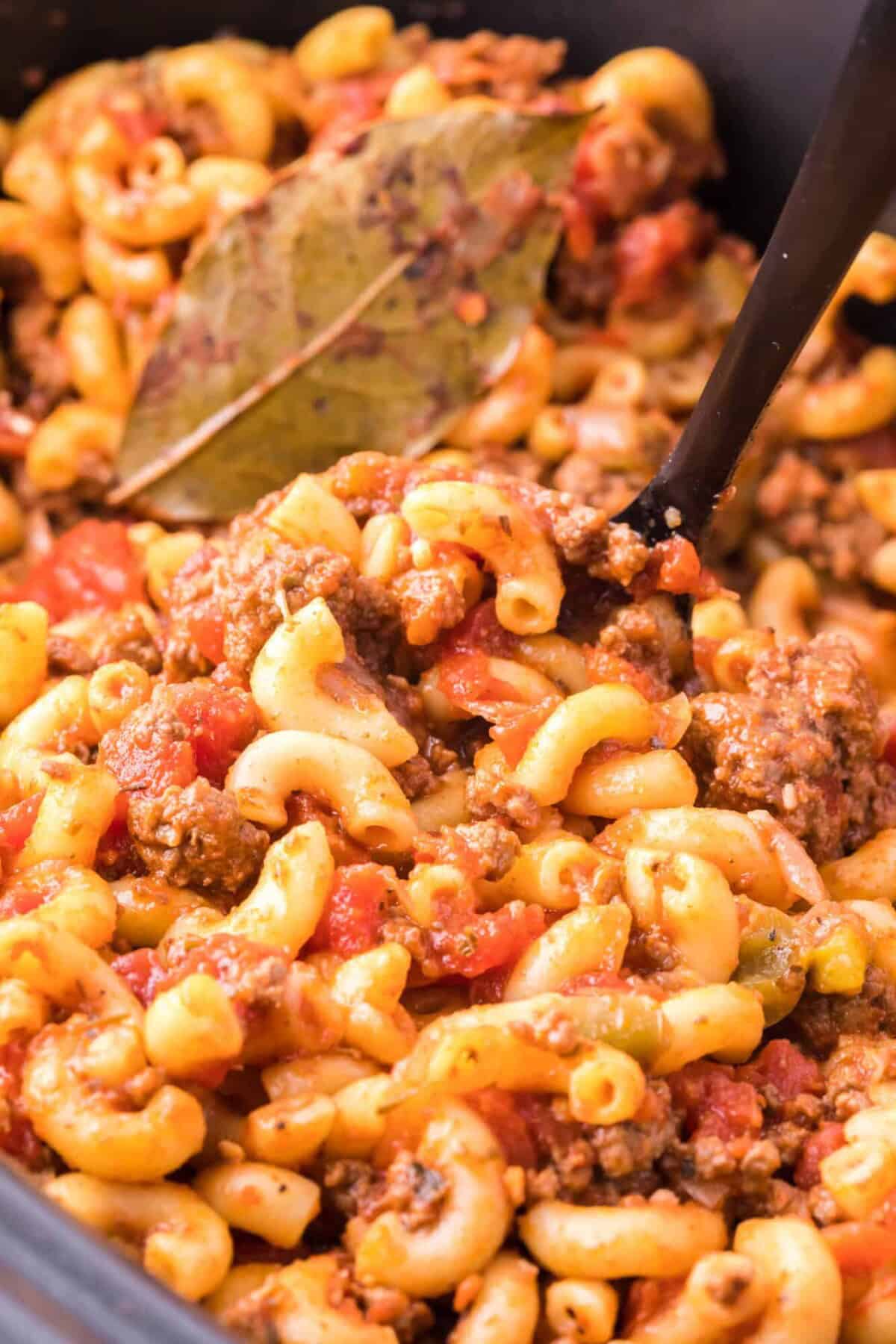 Close up of a serving spoon stuck into goulash inside the crockpot.