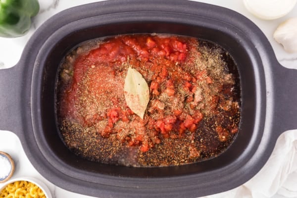 Overhead view of herbs and seasonings added to ground beef and tomato sauce in the crockpot.