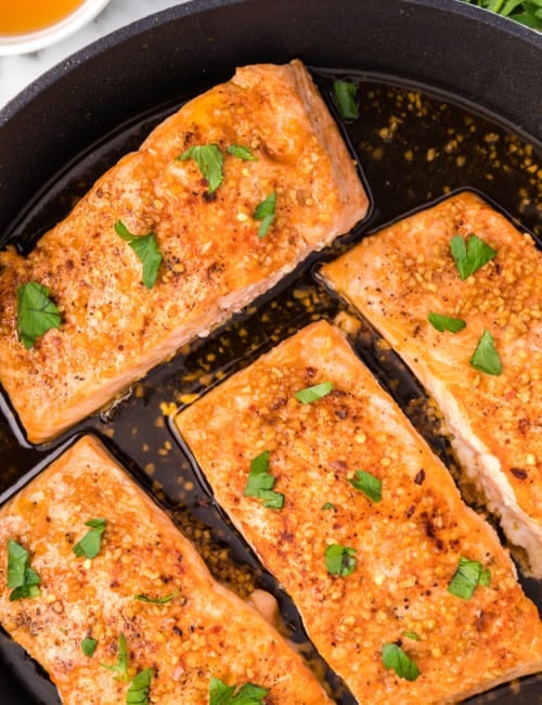 Honey garlic salmon in a frying pan, topped with fresh parsley.