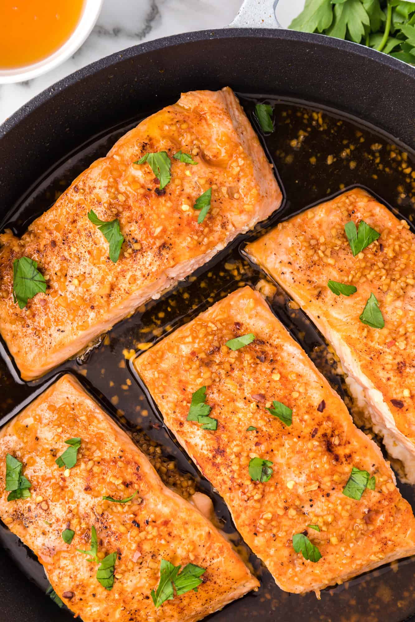 Honey garlic salmon in a frying pan, topped with fresh parsley.