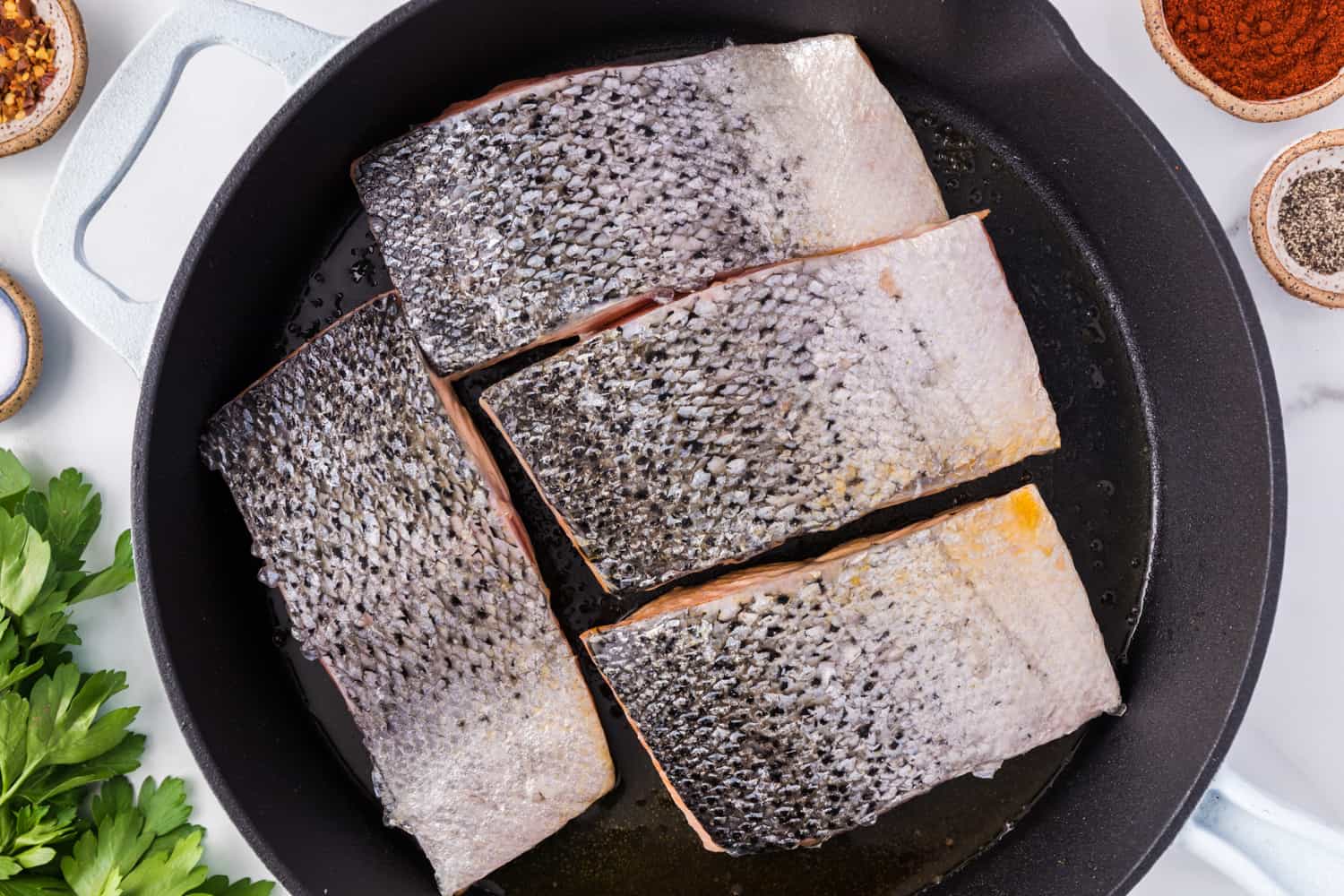 Salmon fillets face down in a frying pan.