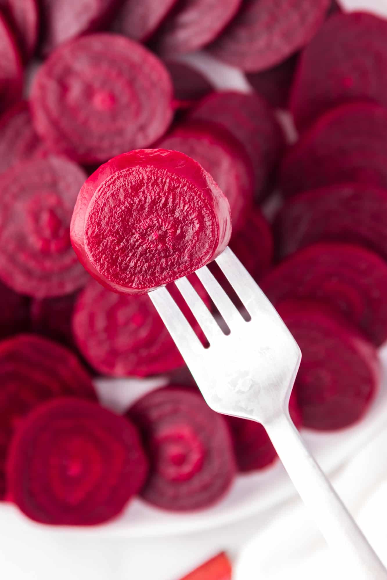 Cooked beet slice on a fork, with more in background.