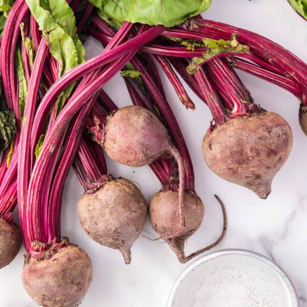 Overhead view of fresh beets with greens attached, and a small measuring cup of water.