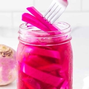 Pickled turnips being lifted from a jar with a fork.