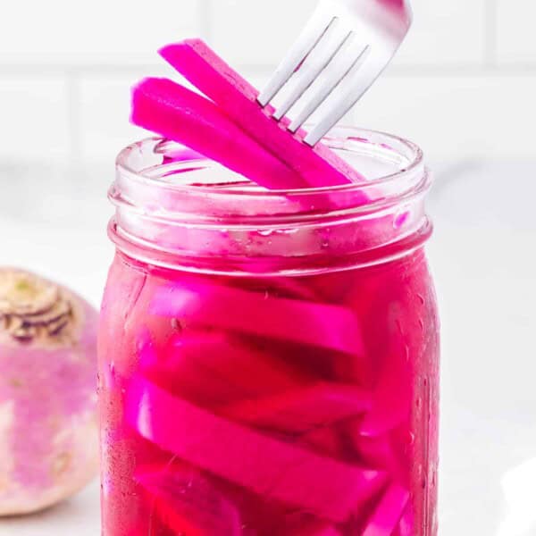Pickled turnips being lifted from a jar with a fork.
