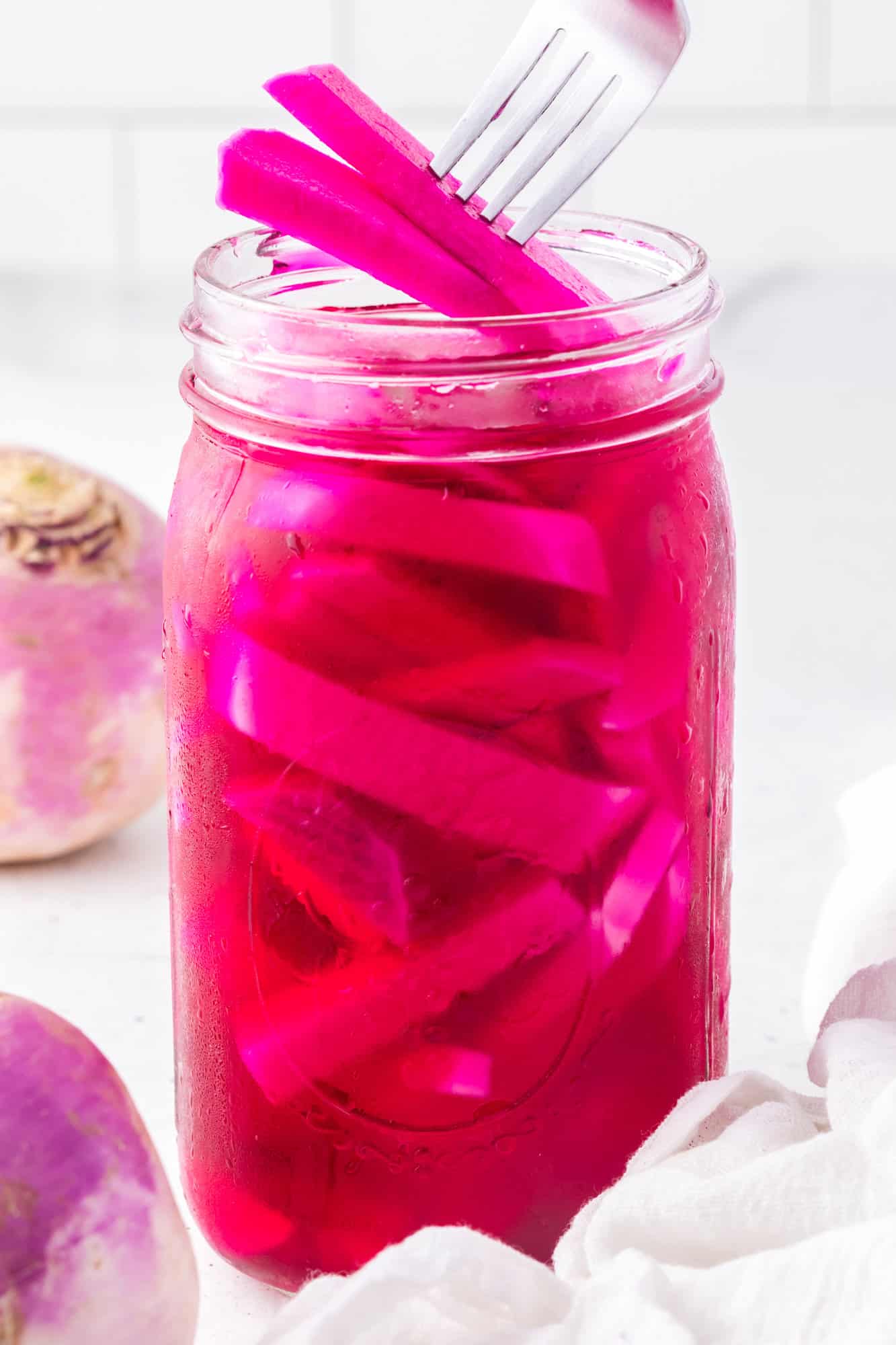 Pickled turnips being lifted out a jar with a fork.