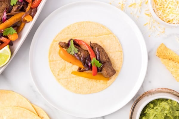 Overhead view of a tortilla topped with steak fajitas on a plate.