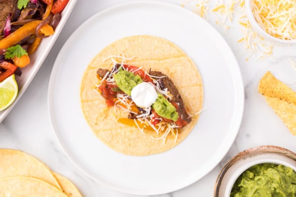 Overhead view of a tortilla topped with steak fajitas and garnishes on a plate.