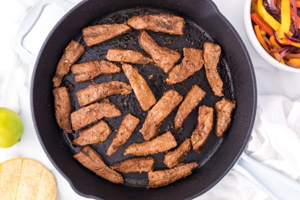 Overhead view of browned steak slices in a skillet.