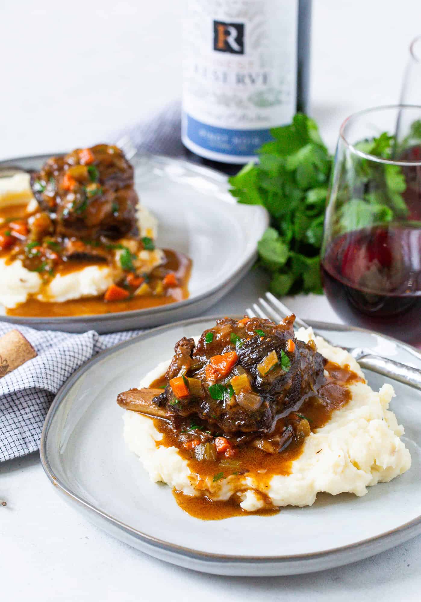 Short ribs on top of mashed potatoes, bottle of wine in the background.