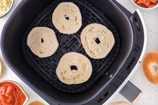 Mini bagel halves in air fryer basket.