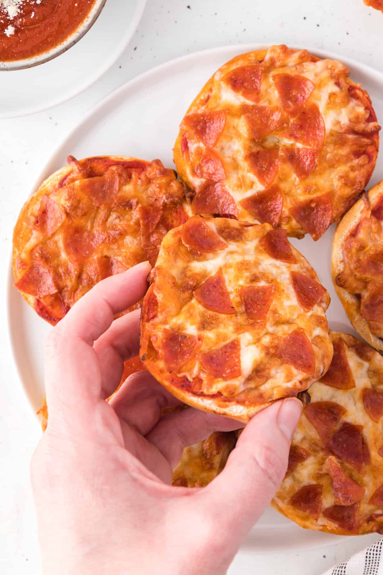 Hand holding a homemade bagel bite pizza.