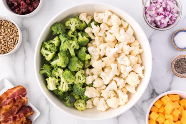 Broccoli and cauliflower florets in a bowl surrounded by salad ingredients.