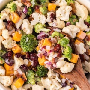 Overhead view of broccoli cauliflower salad in a white bowl with a wooden spoon.