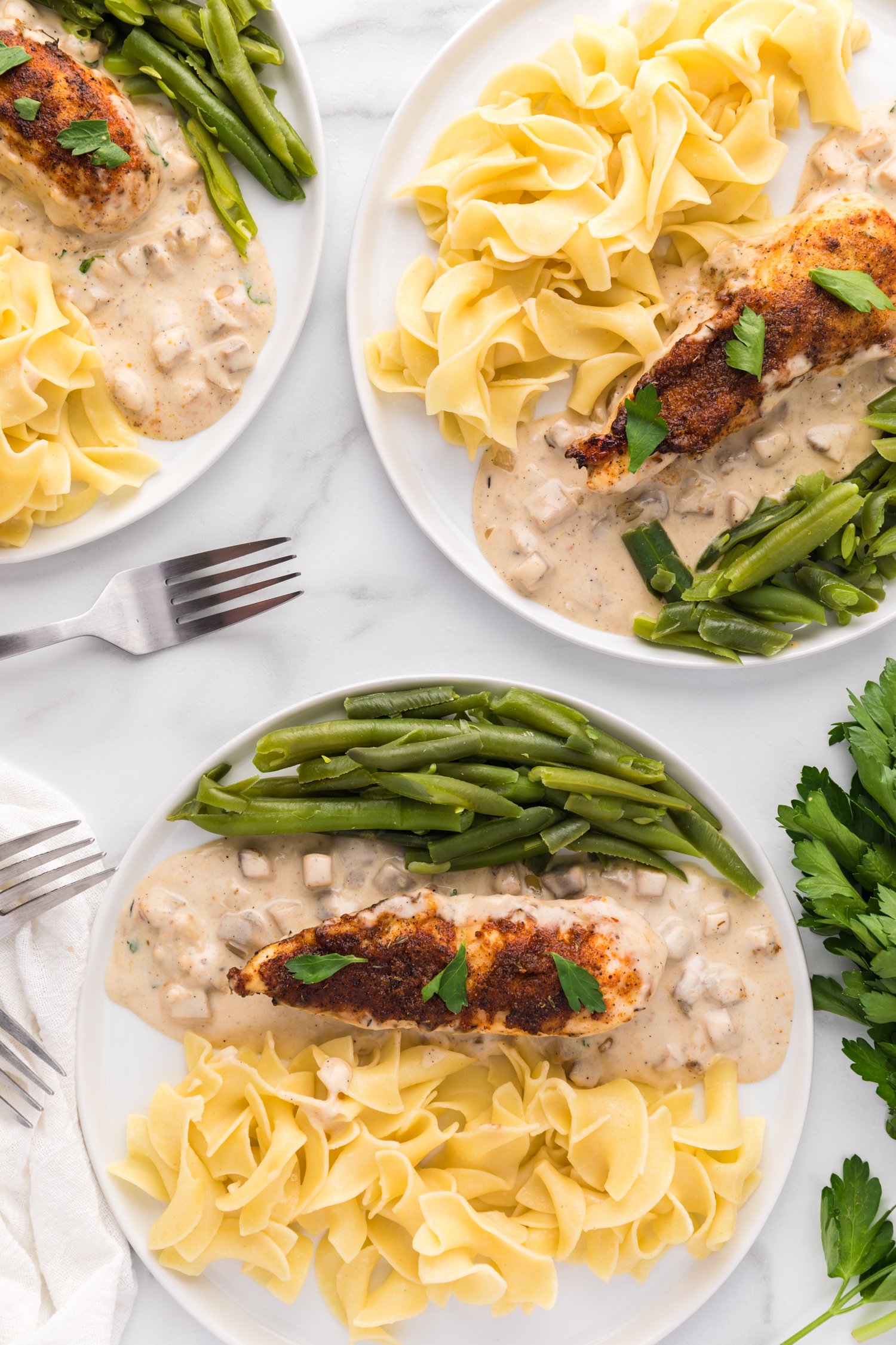 Overhead view of plates of cream of mushroom chicken served over egg noodles with a side of green beans.