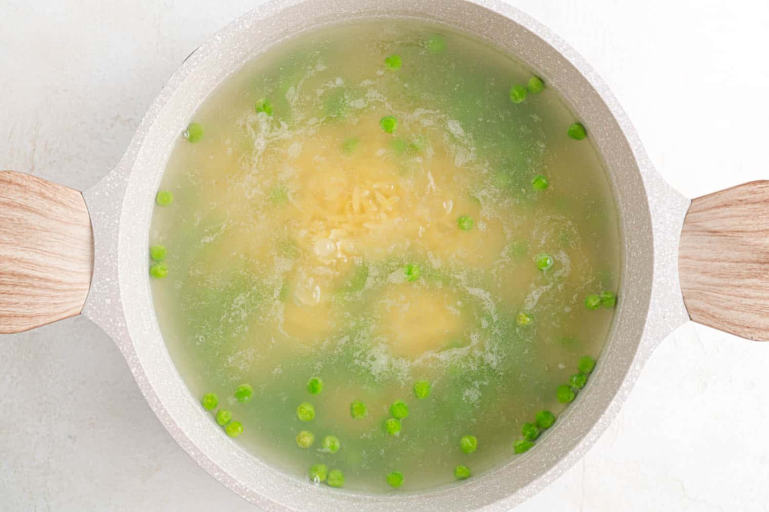 Peas added to pasta and boiling water.