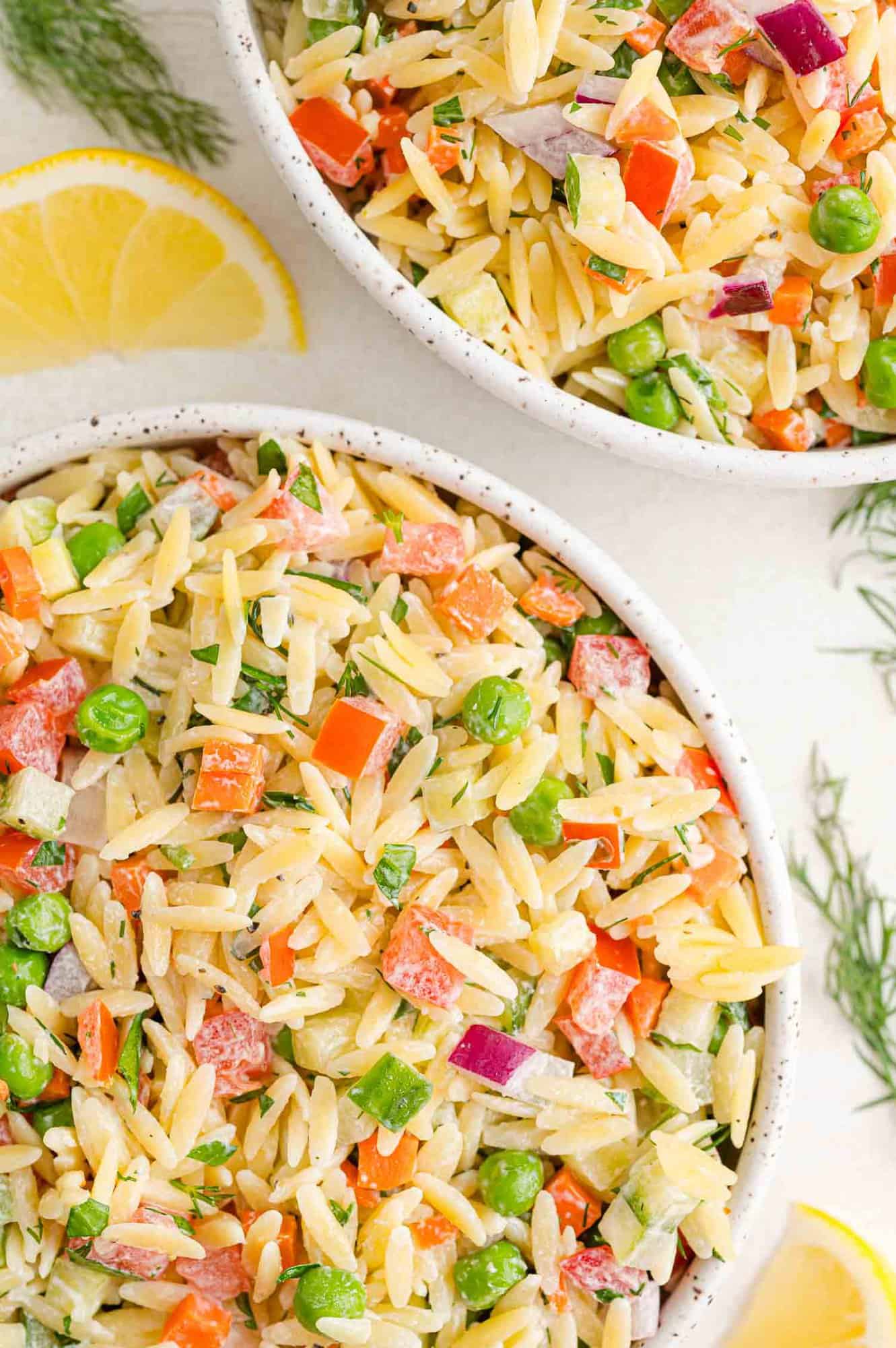 Orzo salad with yogurt dressing in two bowls, with vegetables including peas, onions, tomatoes.