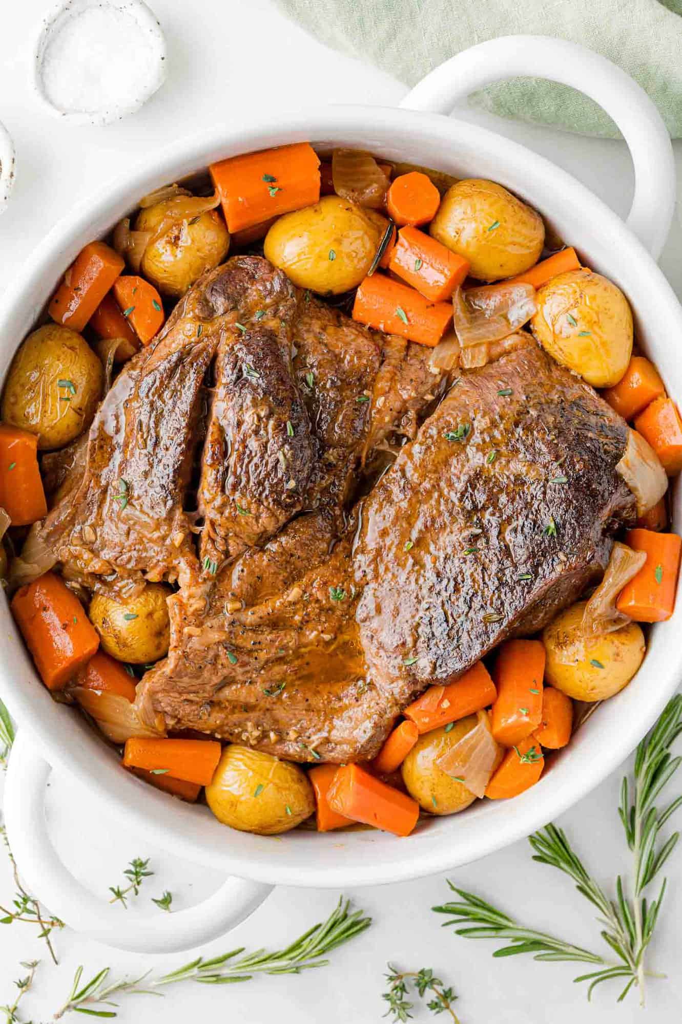 Cooked pot roast in a white pan with potatoes and carrots.
