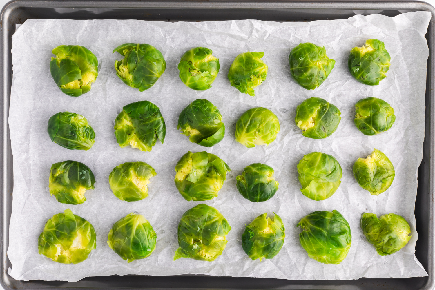 Whole Brussels sprouts on a sheet pan, after being smashed down and flattened slightly.