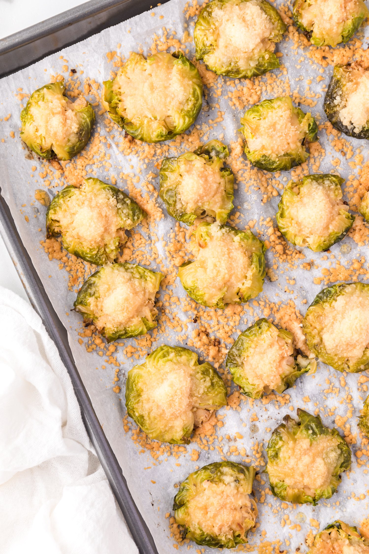 Smashed Brussels sprouts sprinkled with cheese, on a parchment paper lined baking sheet.