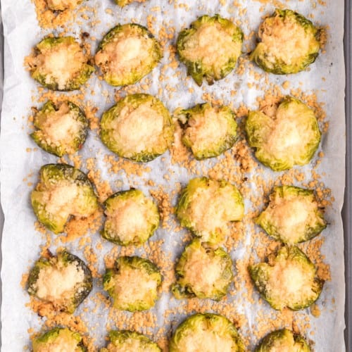 Smashed Brussels sprouts on a sheet pan, sprinkled with cheese.