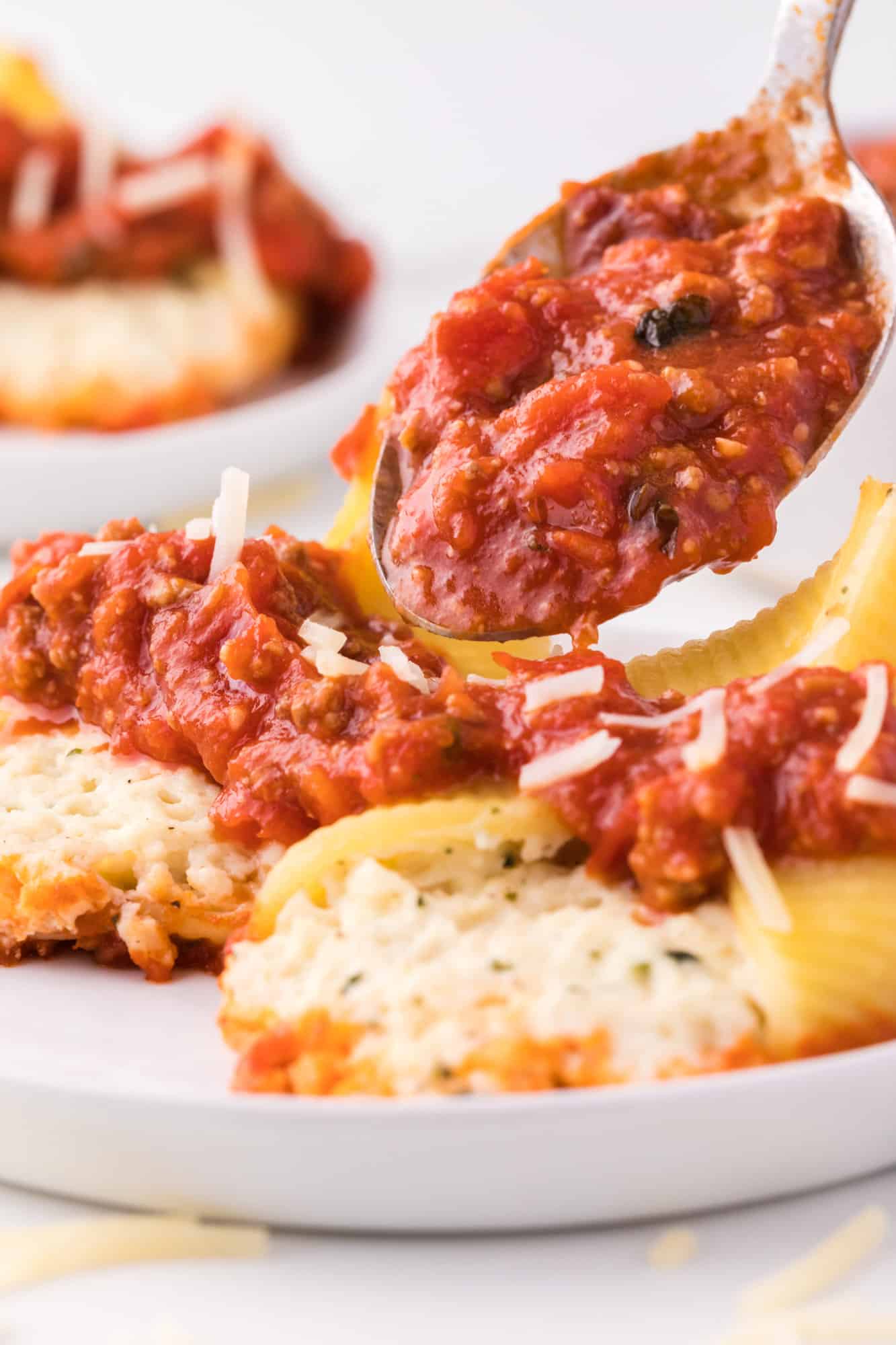 Meat sauce being spooned over cheese stuffed shells.