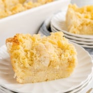 A serving of pineapple stuffing on a white plate with more stuffing in a casserole dish in the background.