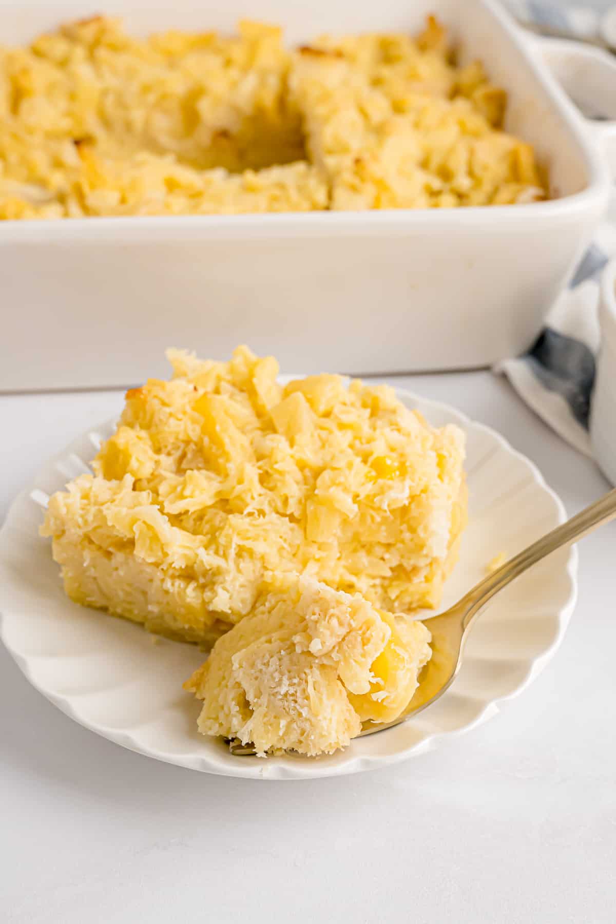 A forkful laying next to pineapple stuffing on a white plate, with more stuffing in a casserole dish in the background.