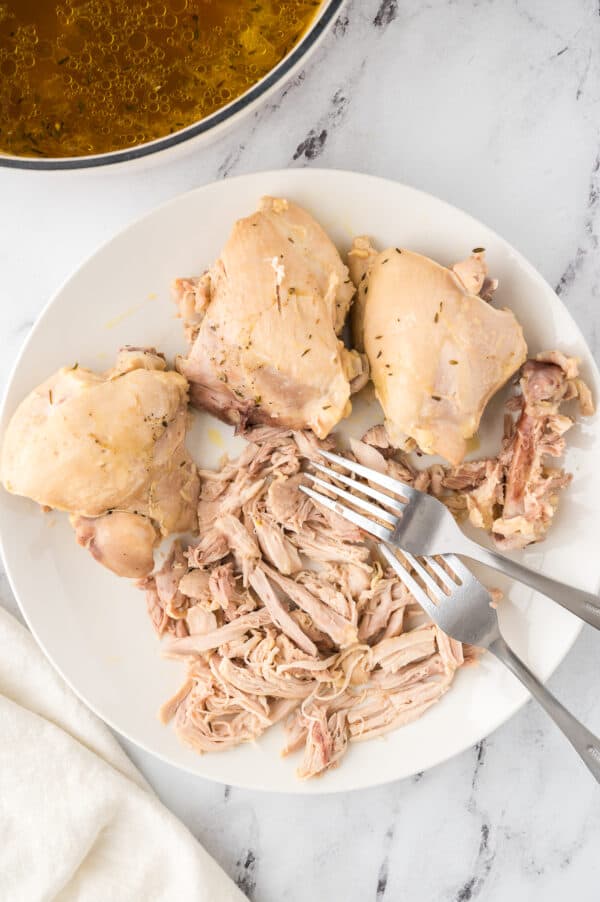 Partially shredded bone-in chicken thighs on a white plate with a fork.