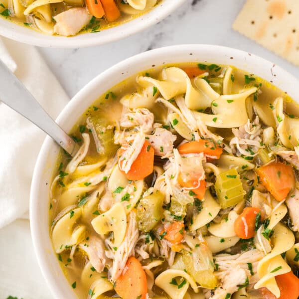 Overhead view of homemade chicken noodle soup in a bowl with a spoon, next to a second bowl of soup.
