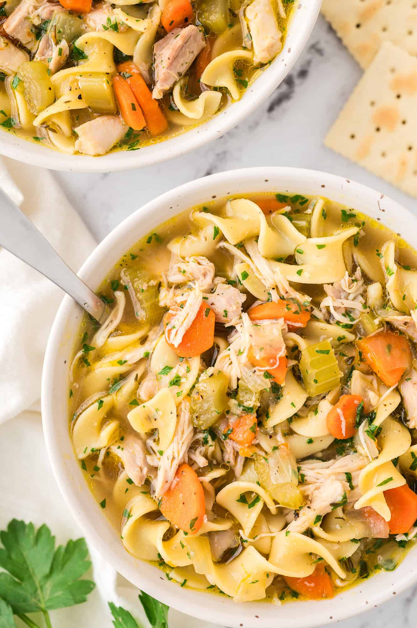 Overhead view of homemade chicken noodle soup in a bowl with a spoon, next to a second bowl of soup.