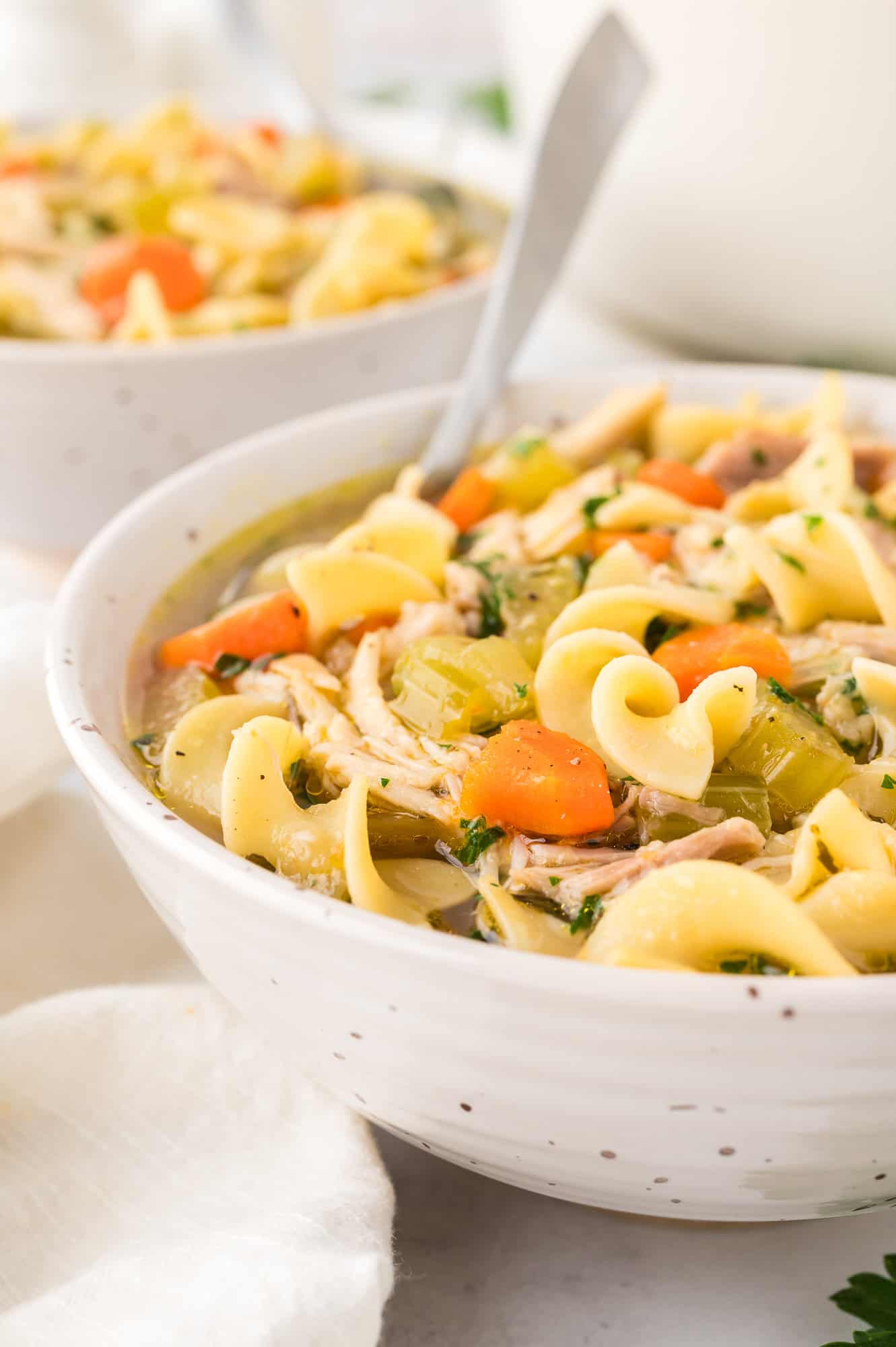 A bowl of chicken noodle soup with a second bowl of soup in the background.