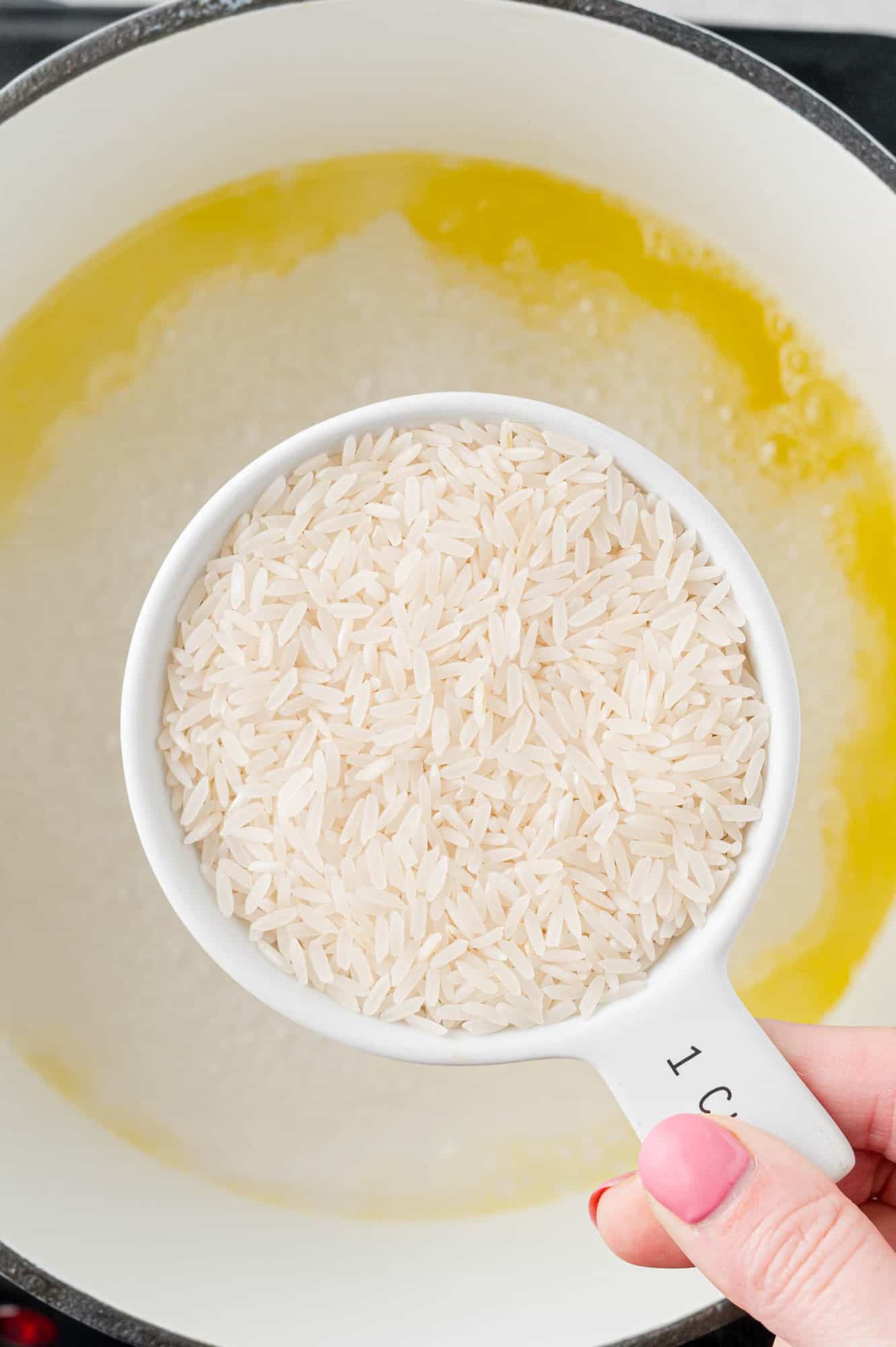 Rice being held in a measuring cup above pan.