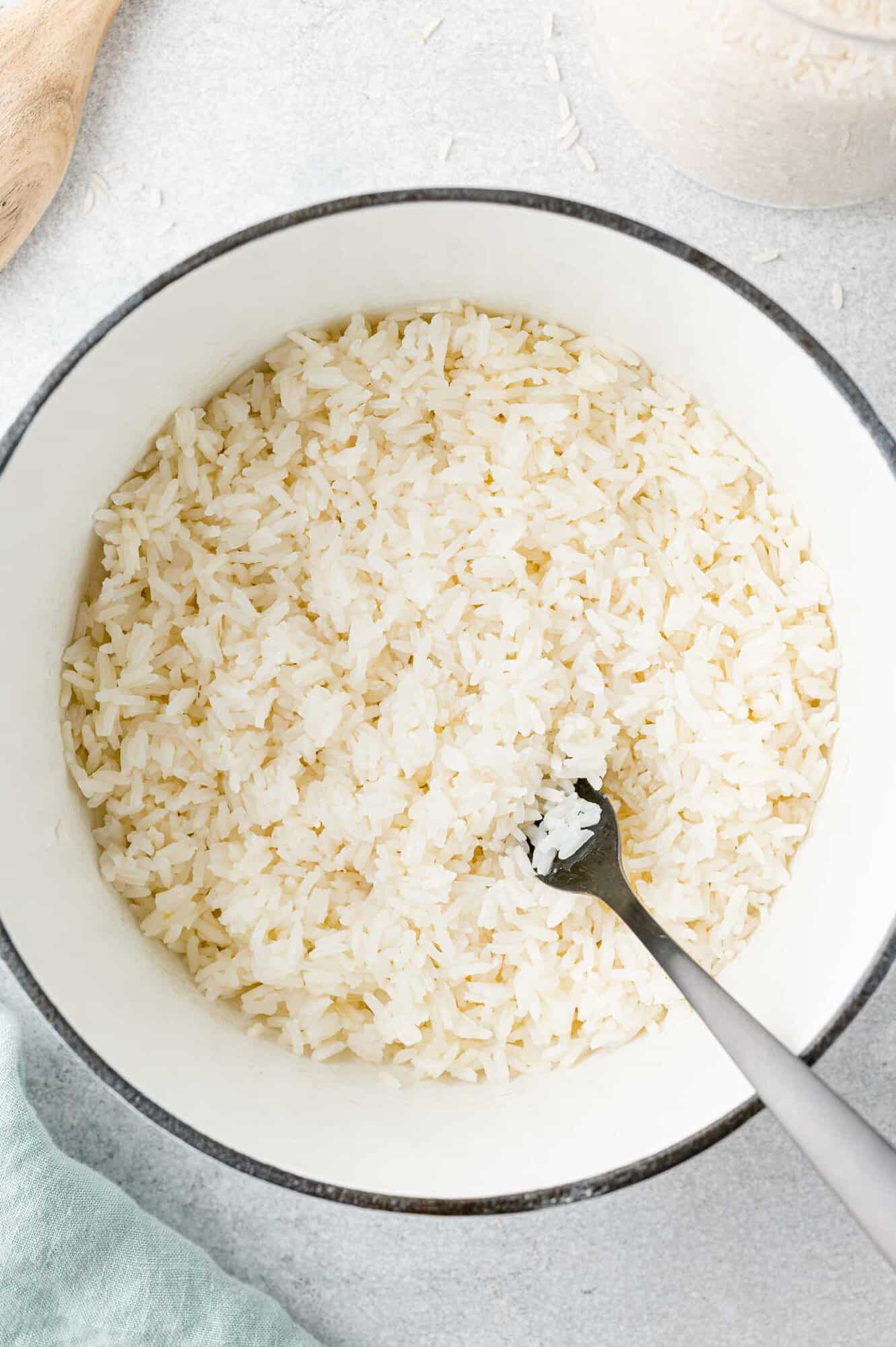 Cooked jasmine rice in pan with a fork fluffing it.