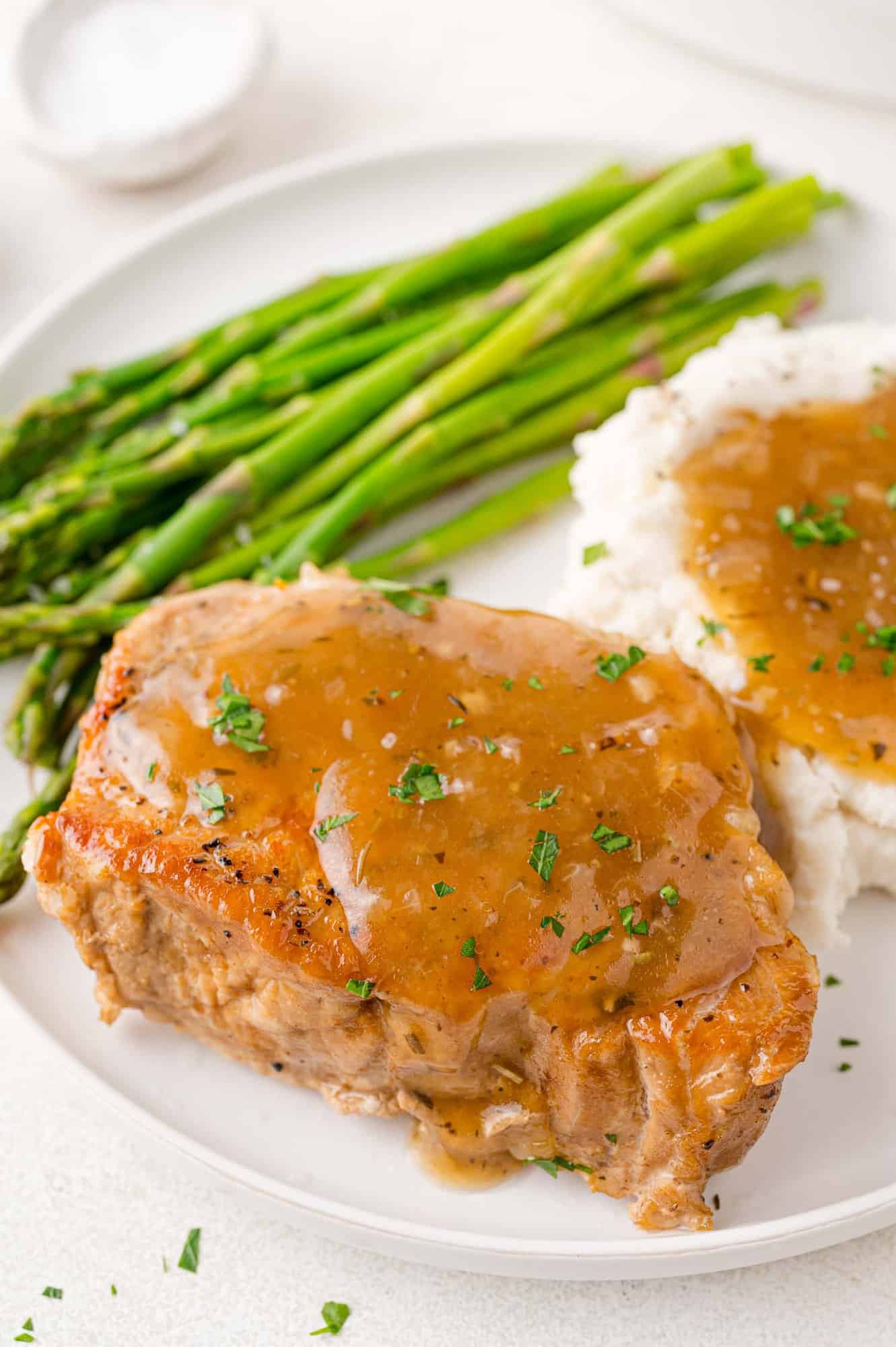 Pork chop and gravy on a plate, with mashed potatoes and asparagus.