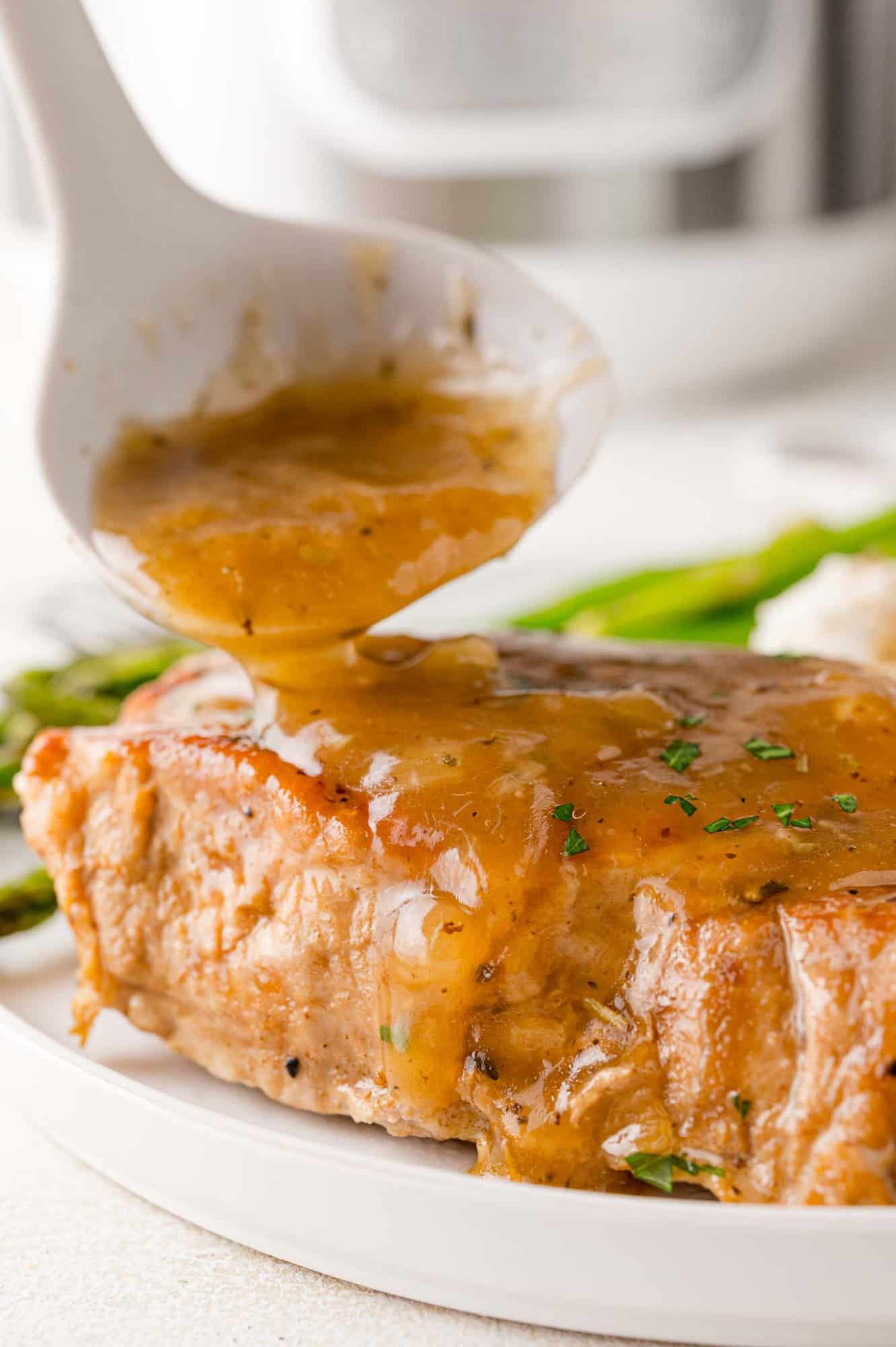 Gravy being poured on pork chop.