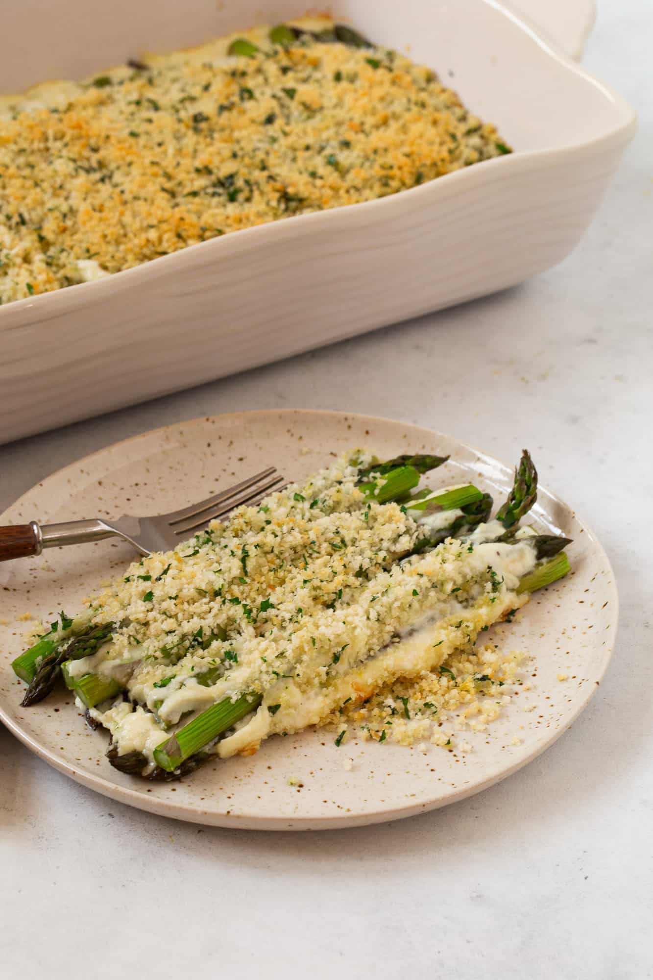 Plated asparagus casserole, with more of the casserole in the background.