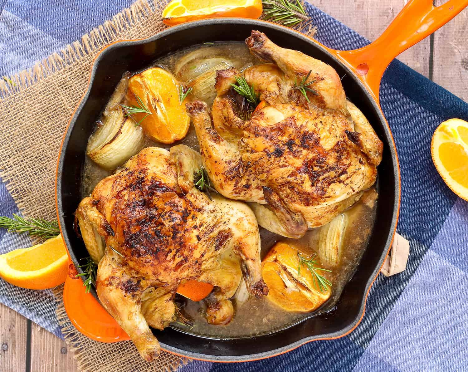 Overhead view of two cornish game hens in a orange skillet, with orange slices.