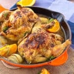 Two cornish game hens in a orange skillet.