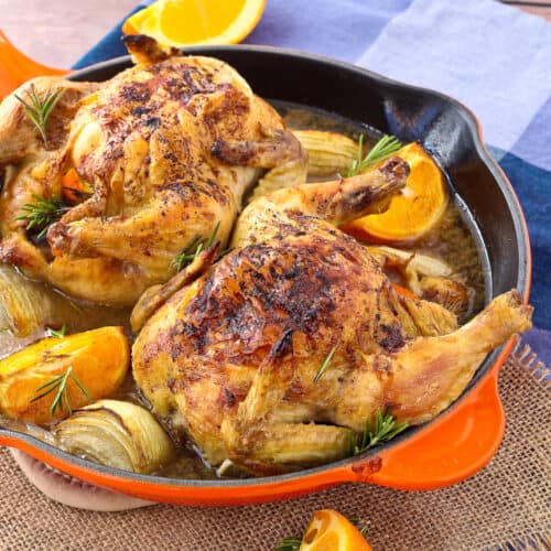 Two cornish game hens in a orange skillet.
