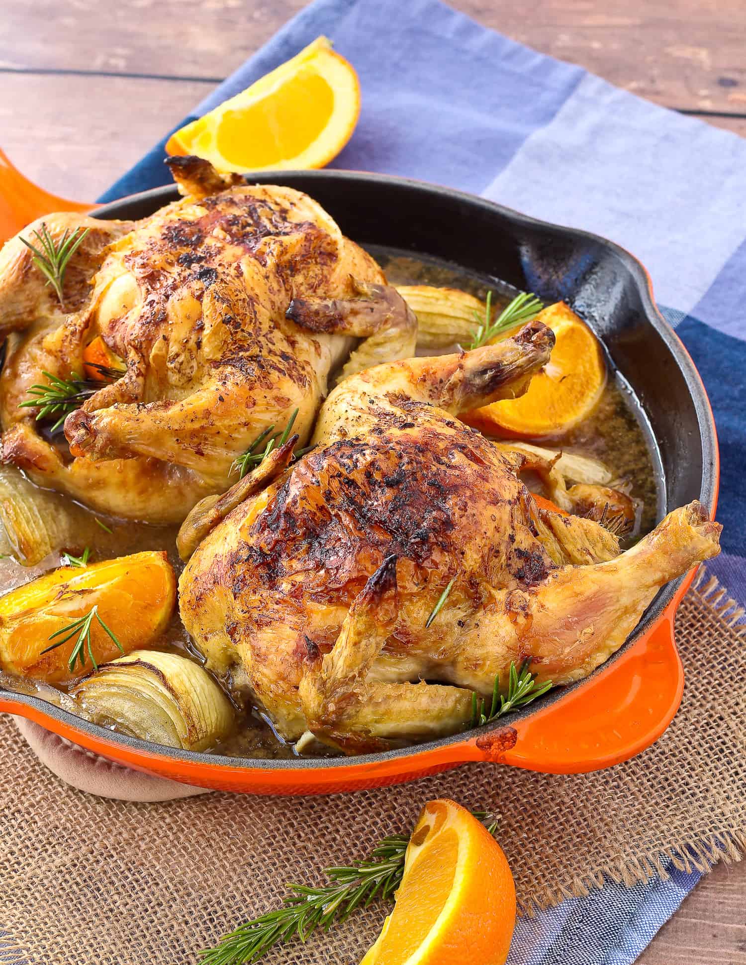 Two cornish game hens in a orange skillet.