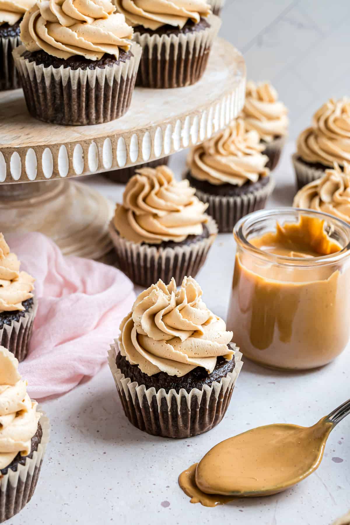 Peanut butter frosting piped on a number of chocolate cupcakes, some on a cake stand.