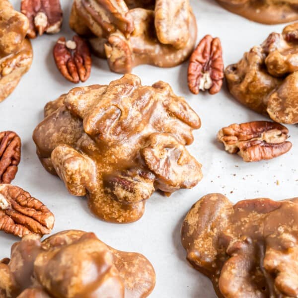 Pecan Pralines on a white surface, surrounded by pecans.