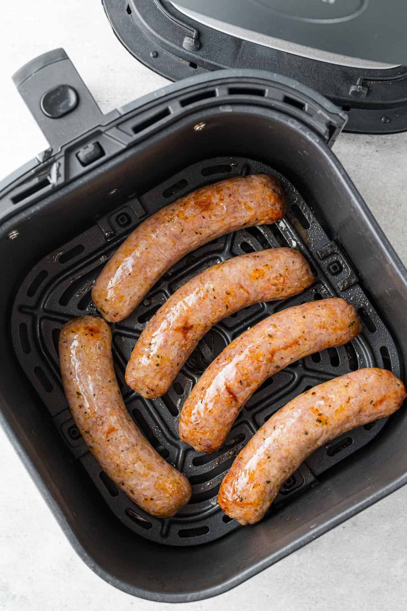 Overhead view of cooked Italian sausage in air fryer basket.