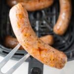 Air fryer Italian sausage held over an air fryer with more in it.