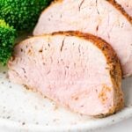 Sliced air fryer pork tenderloin, broccoli in corner of photo.