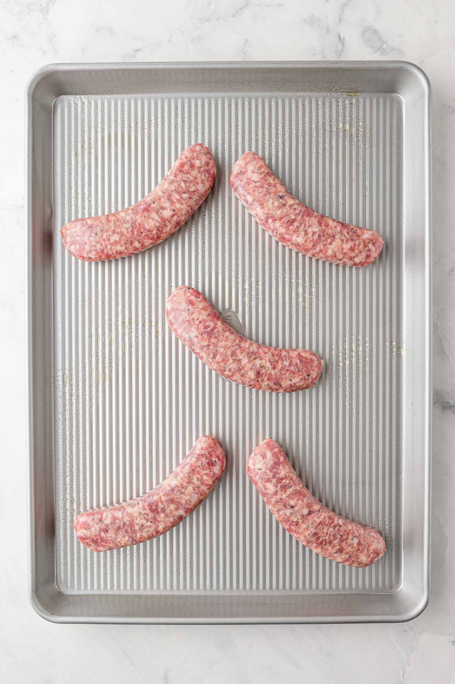 Raw sausages on a sheet pan.